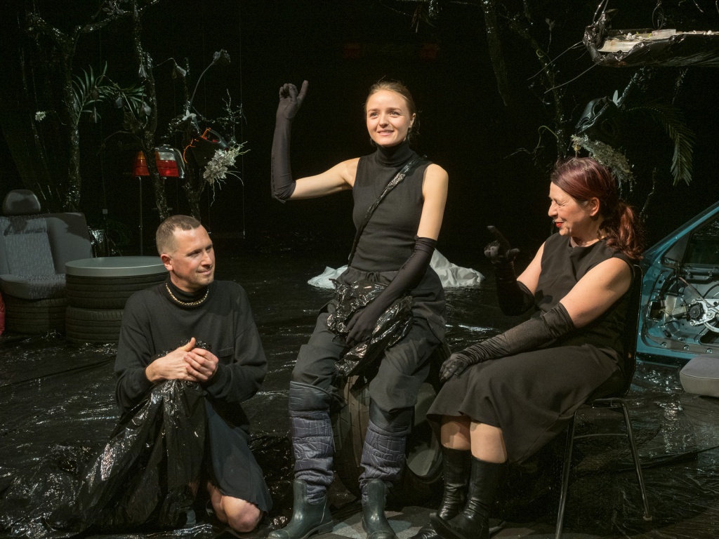 Three actors in black on a dark stage
